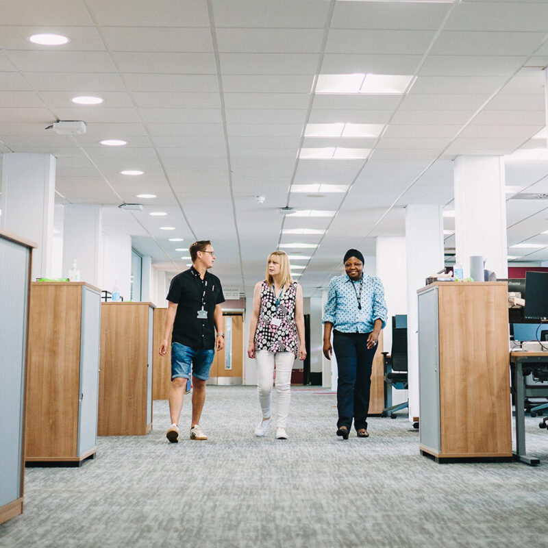 Three staff members walk through one of ONS's spacious brightly lit open plan offices.